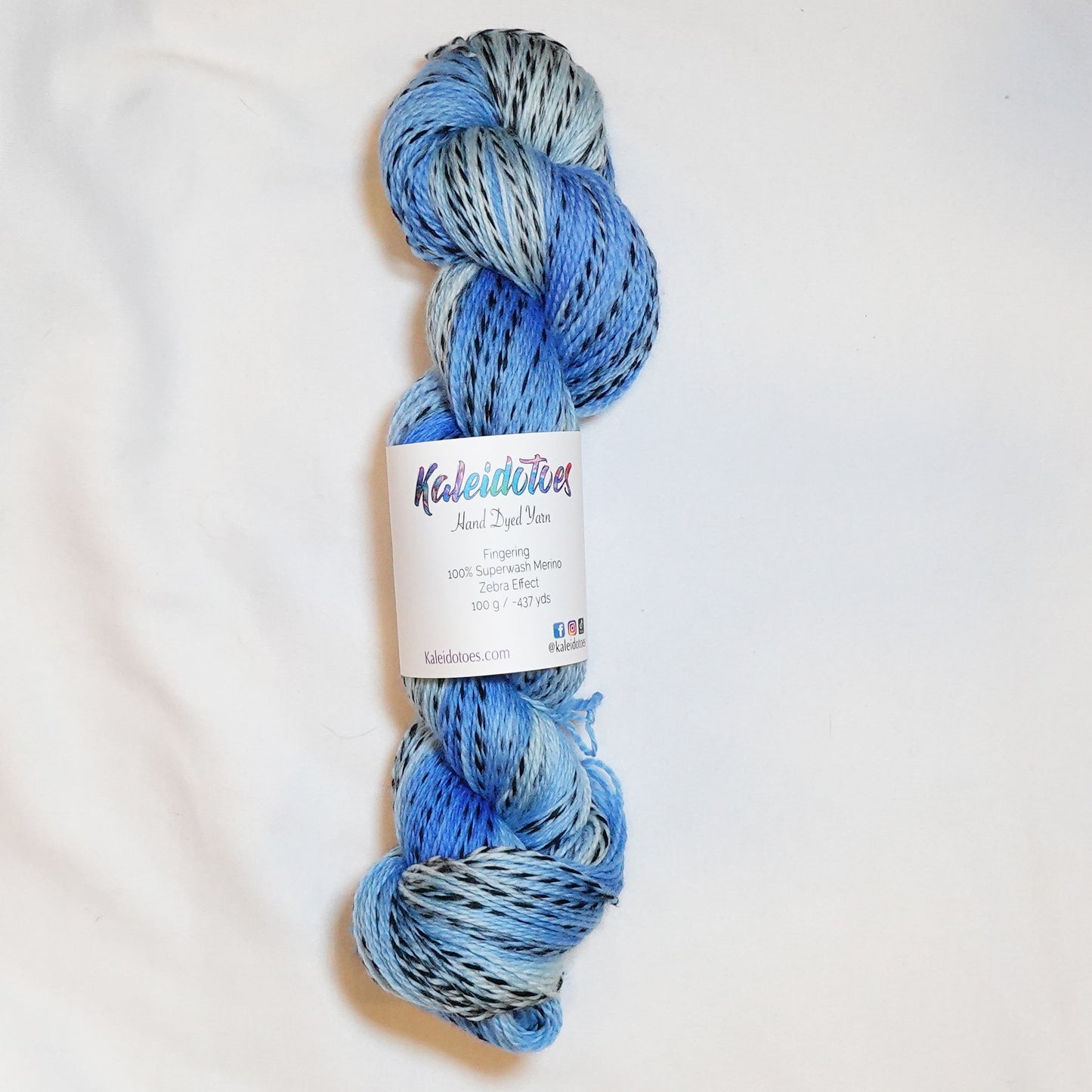 Hand-dyed fingering weight yarn in sand, sage, sky blue, and olive with black threading throughout on a zebra base.