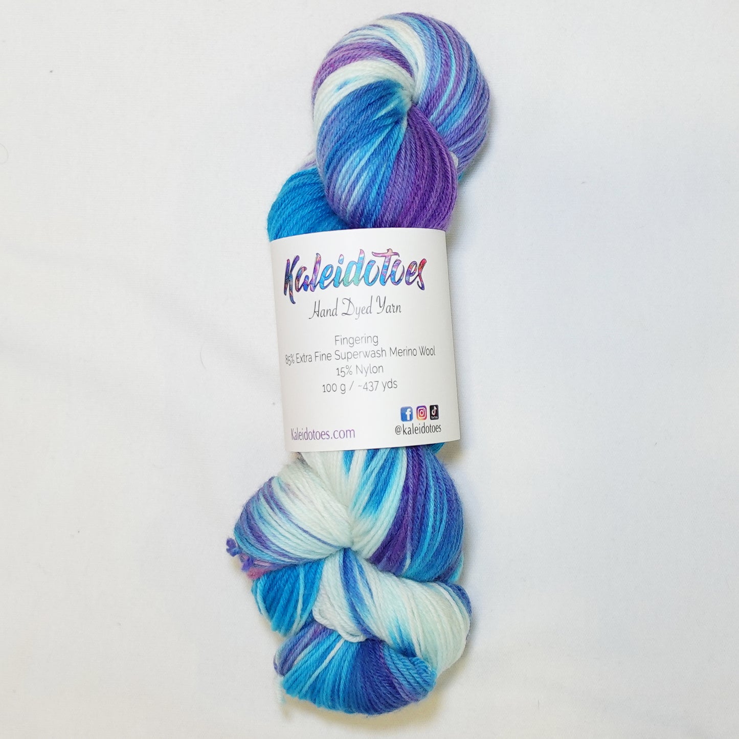 Hand-dyed fingering weight yarn in brilliant blue, soft mint, white, deep violet, and pink with swirling tie-dye color movement throughout.
