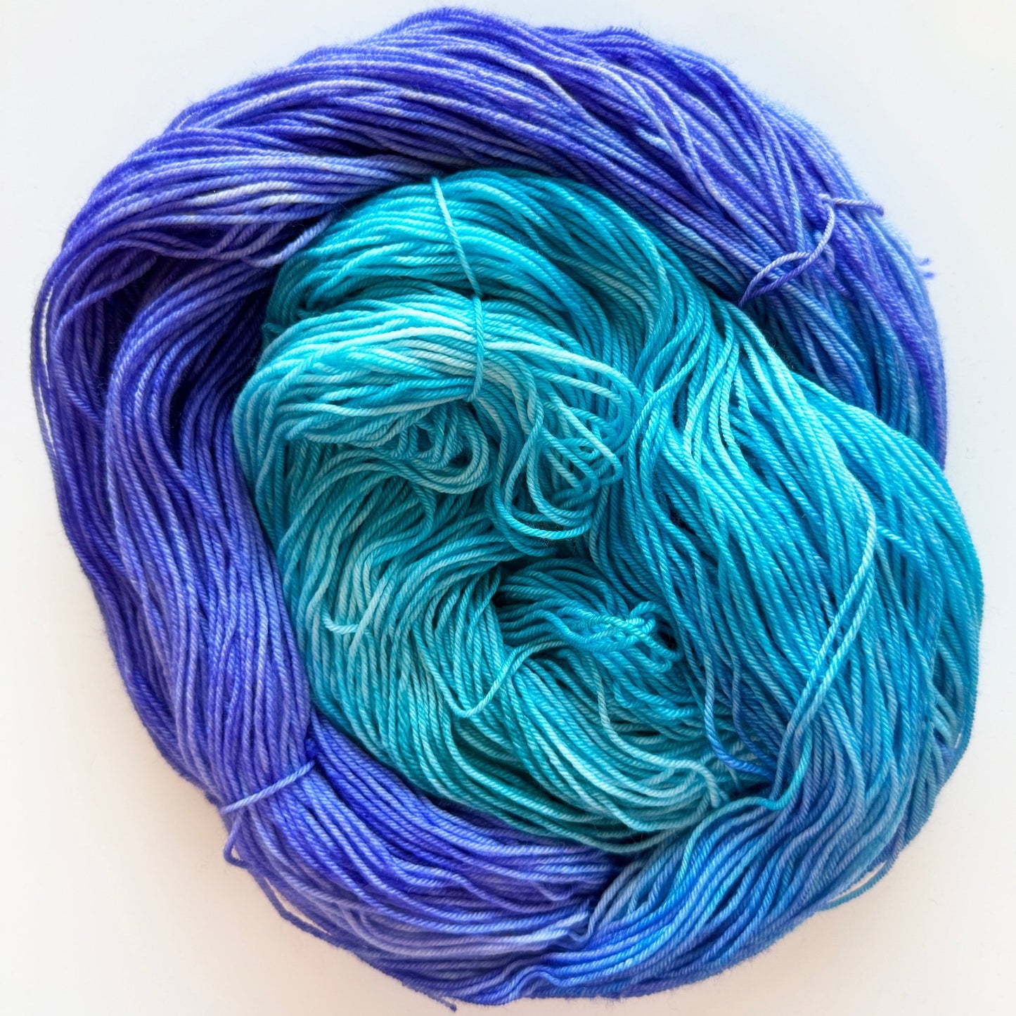 Hand-dyed sock yarn in turquoise, purple, and dusky blue undertones, Indigo Drift colorway.