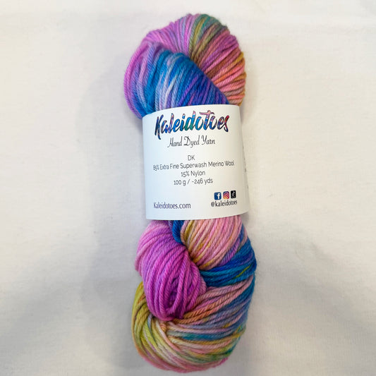 Hand-dyed yarn in shades of turquoise, pink, peach, and orchid — glowing like a tropical sunset over calm water.