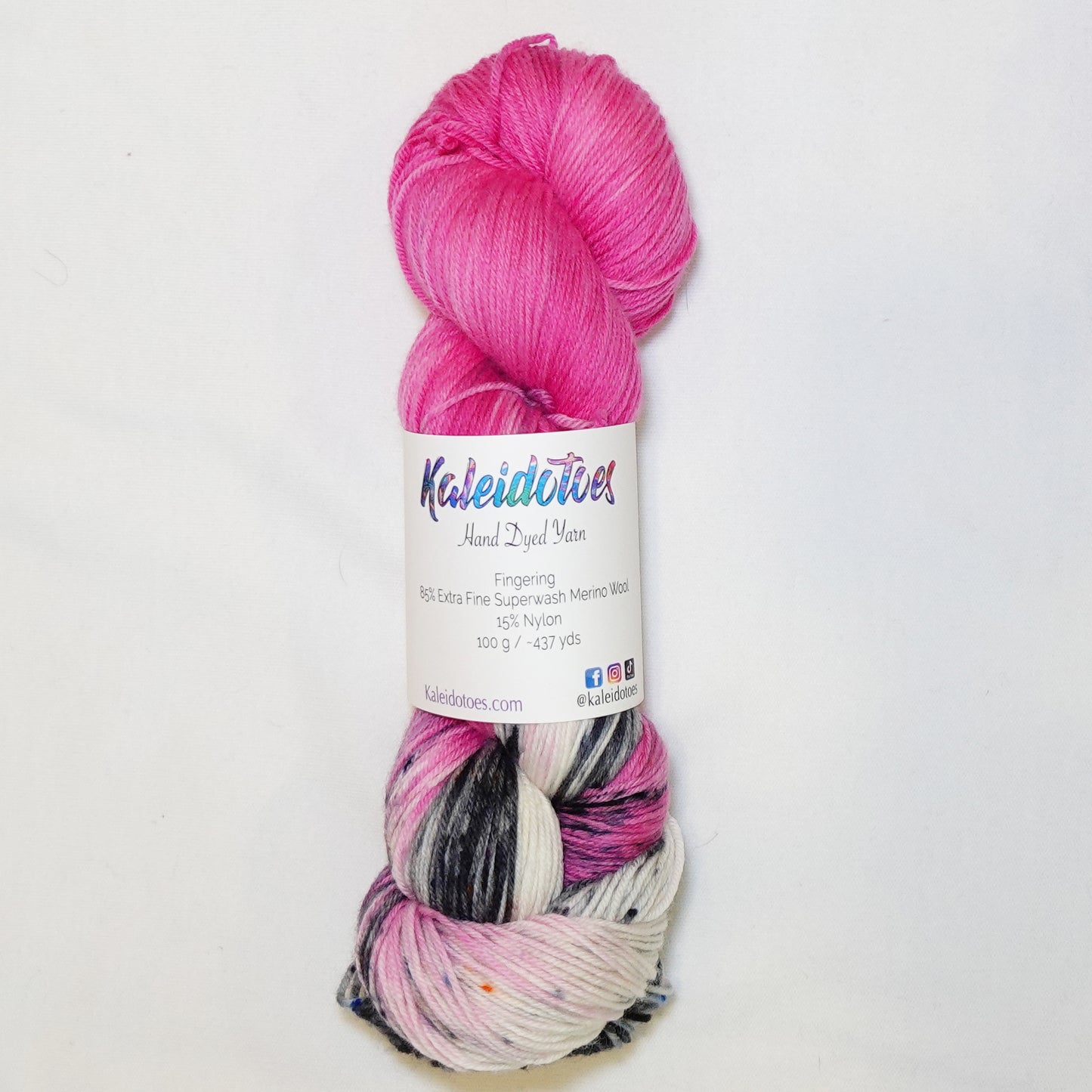 Hand-dyed fingering weight yarn in hot fuchsia pink with black, white, and grey speckled sections throughout.