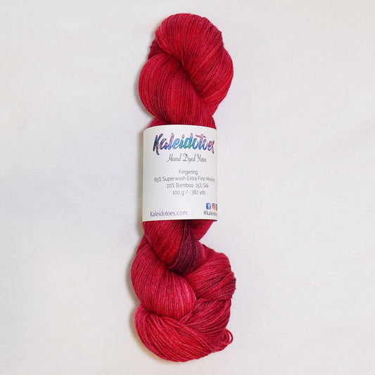 Hand-dyed fingering weight yarn in deep jeweled red with soft violet tones throughout.