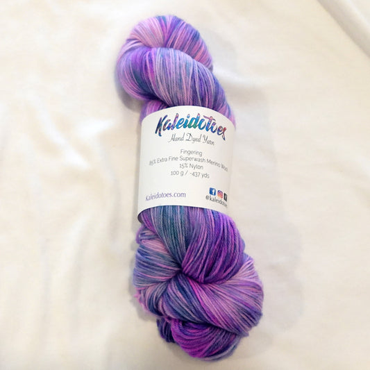 Hand-dyed fingering weight yarn in lavender, orchid, violet, and cool periwinkle with flowing variegated movement.