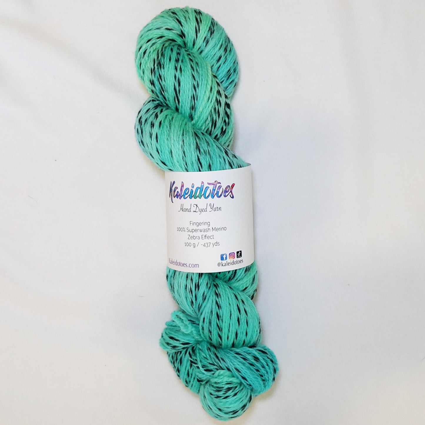 Hand-dyed fingering weight yarn in bright turquoise-teal with aqua and green undertones and black twisted through throughout.