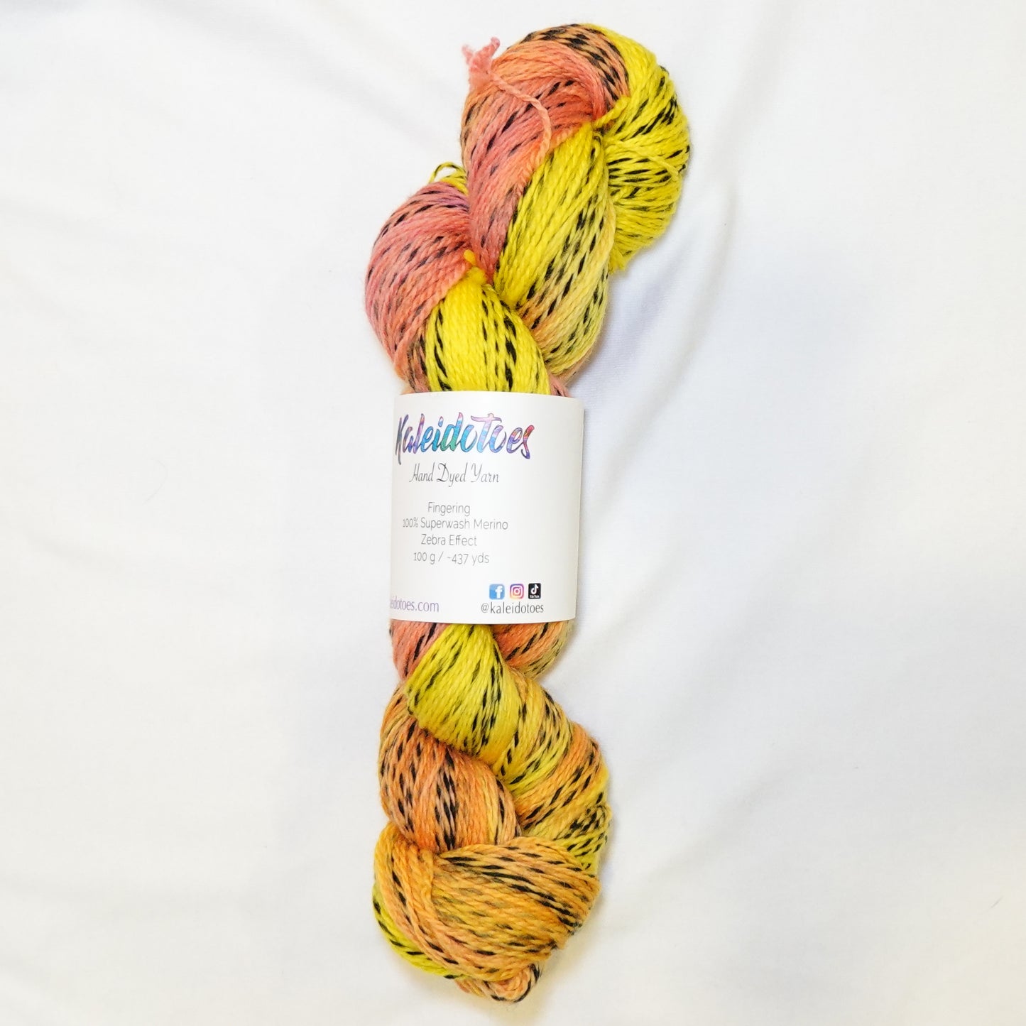 Hand-dyed fingering weight yarn in bright lemon yellow, warm peach, and coral with black twisted through throughout.