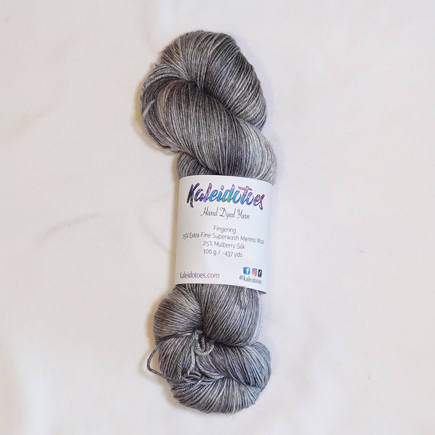 Hand-dyed fingering weight yarn in weathered stone gray, pale blue-gray, soft taupe, and dusty fawn tones.