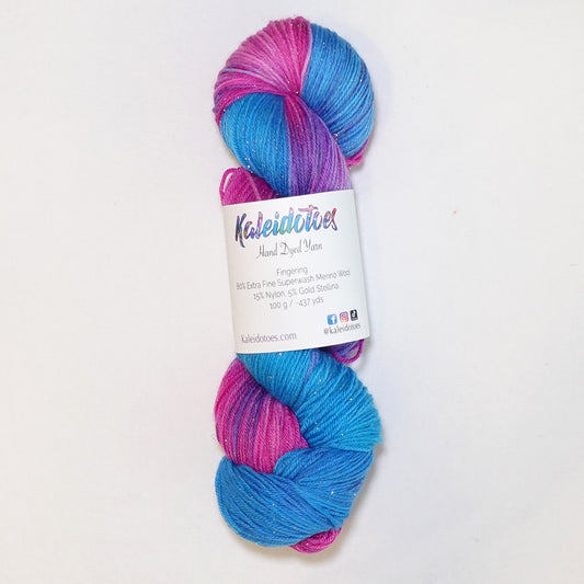 Hand-dyed yarn in vibrant blue, pink, and violet tones with gold metallic running throughout — bright, whimsical, and full of movement.