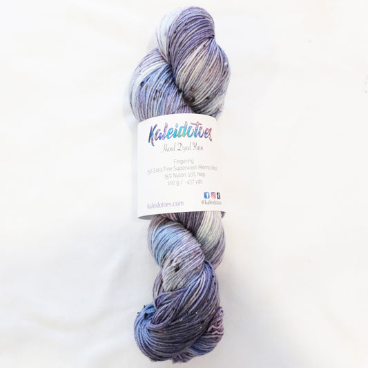 Hand-dyed tweed yarn in dusty mauve and soft grey-blue — muted, atmospheric, and quietly complex with subtle flecks throughout.