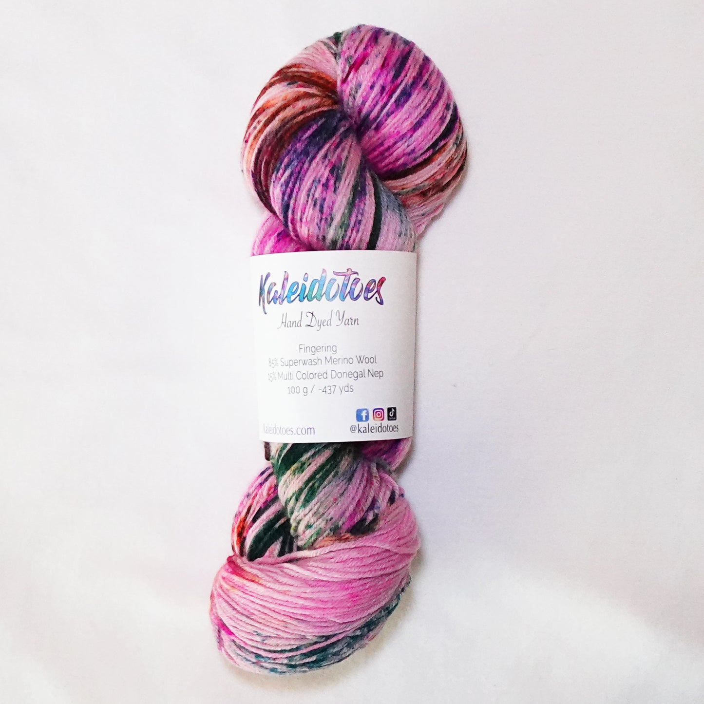 Hand-dyed fingering weight yarn in pink with deep evergreen sections and orange and violet speckles throughout.