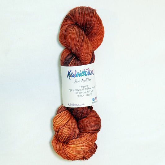 Hand-dyed fingering weight yarn in warm reddish-brown with coppery highlights and deep rust tones.
