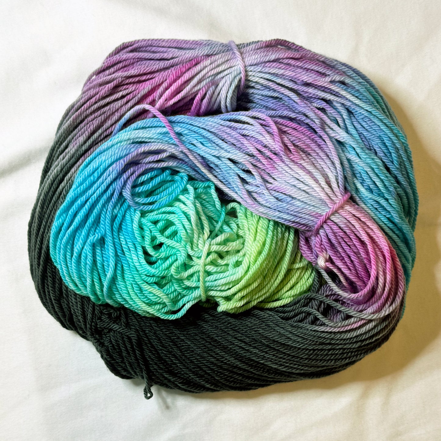 Hand-dyed skein of worsted weight yarn in deep charcoal, lavender, soft pink, turquoise, and seafoam green — luminous and layered like stained glass.
