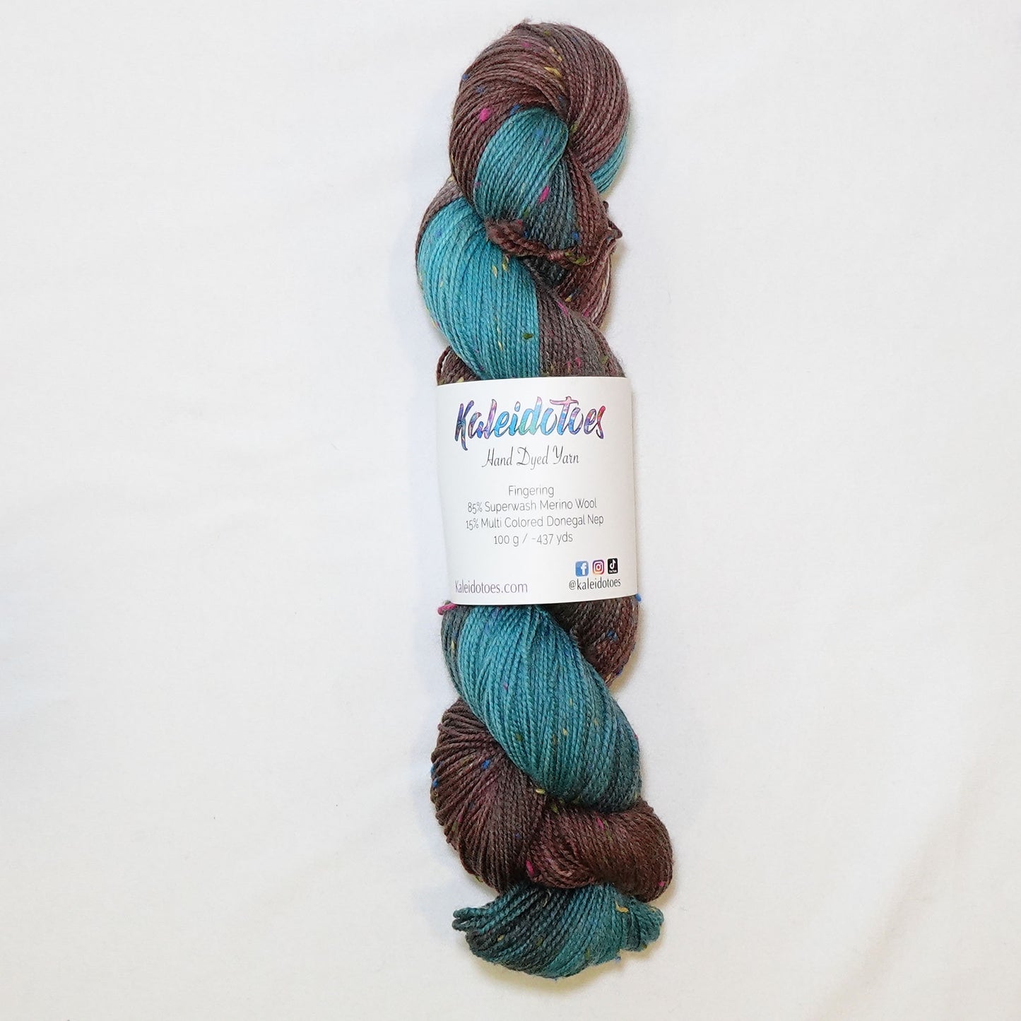 Hand-dyed fingering weight yarn in deep chocolate and bright teal with charcoal transitions and multicolor confetti flecks throughout.