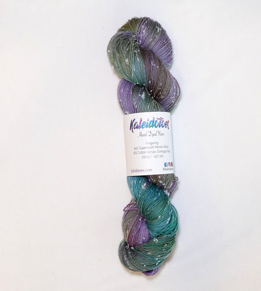 Hand-dyed yarn in moody green, olive, and muted violet tones with soft white flecks — earthy, atmospheric, and softly blended.