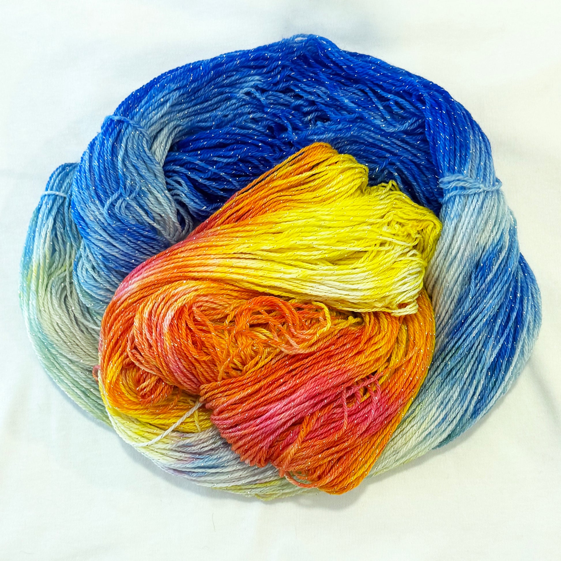 Hand-dyed yarn in sapphire blue, gold, orange, and ivory tones with subtle silver metallic throughout.
