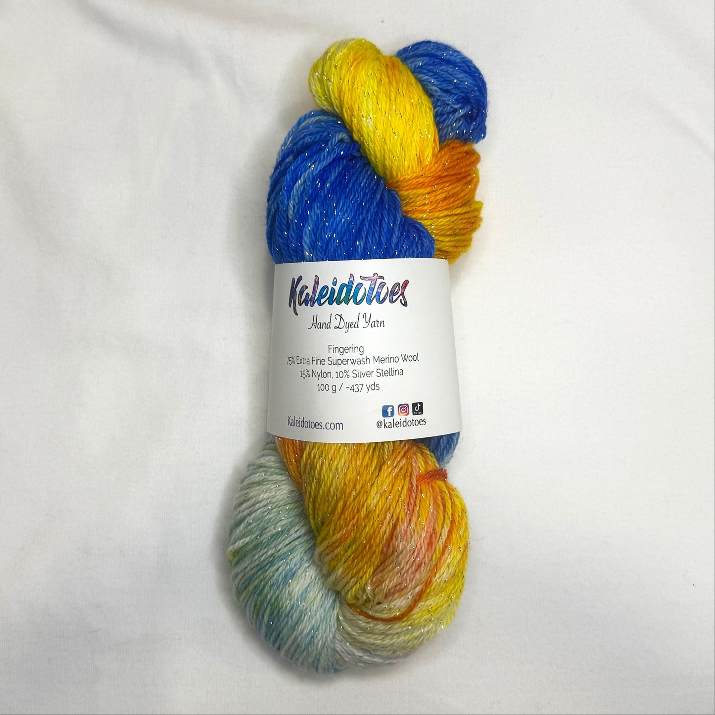 Hand-dyed yarn in sapphire blue, gold, orange, and ivory tones with subtle silver metallic throughout.