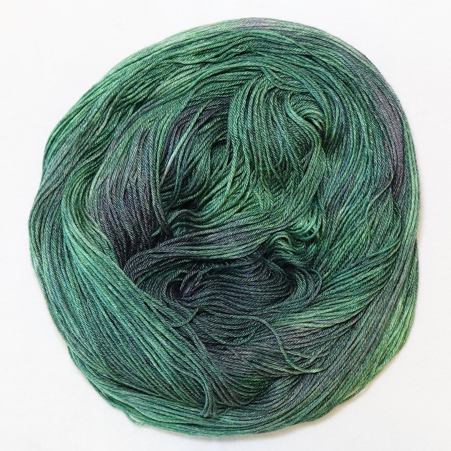 Hand-dyed fingering weight yarn in deep emerald and pine green with shadowy violet tones throughout.