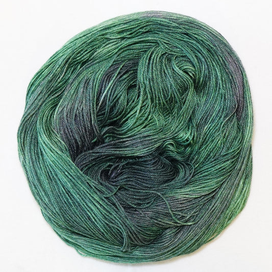 Hand-dyed fingering weight yarn in deep emerald and pine green with shadowy violet tones throughout.