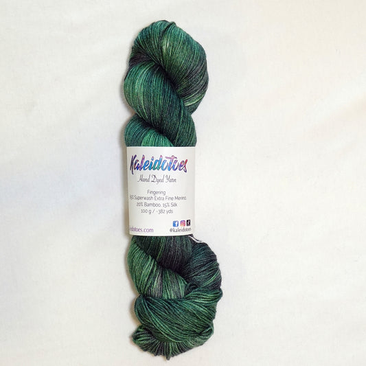 Hand-dyed fingering weight yarn in deep emerald and pine green with shadowy violet tones throughout.