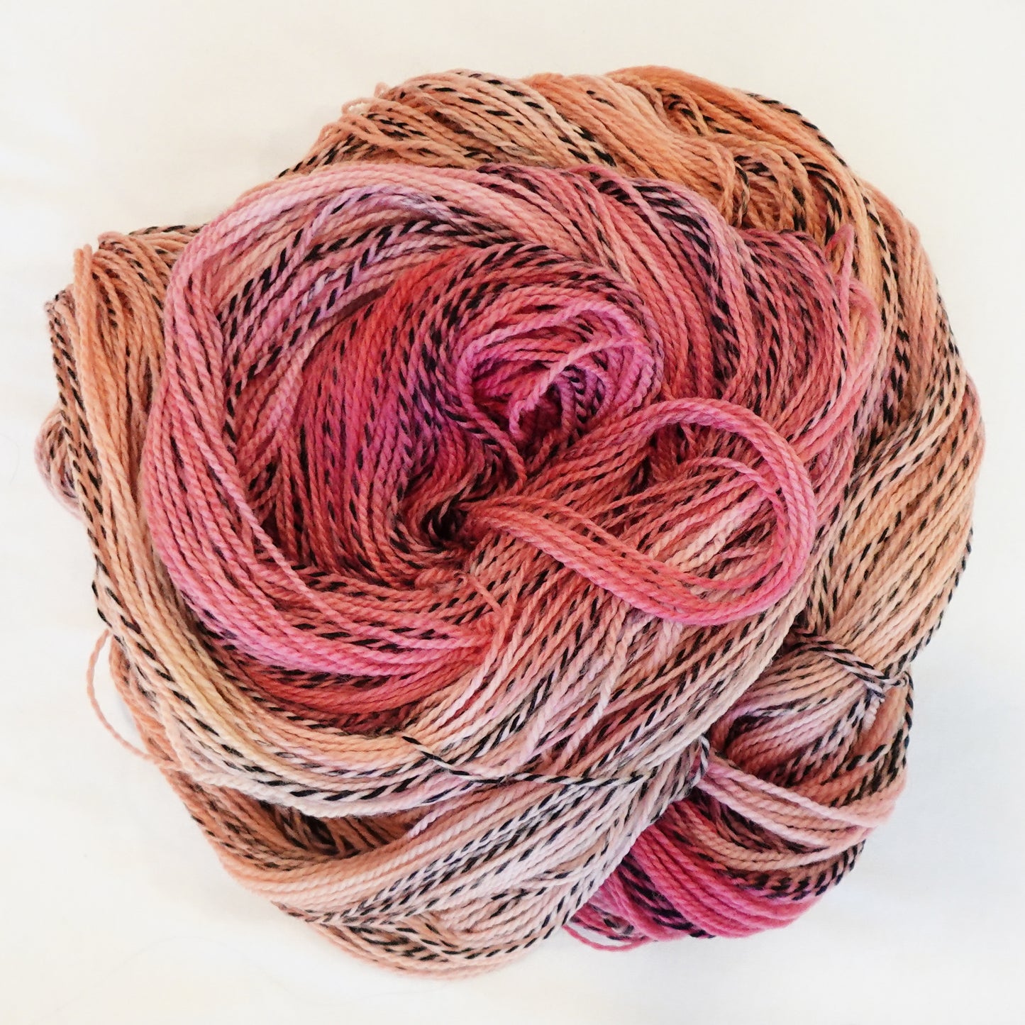 Hand-dyed fingering weight yarn in soft peachy-pink, warm peach, and dusty coral with black twisted through throughout.
