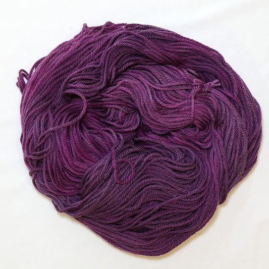 Hand-dyed worsted weight yarn in deep plum and eggplant tones with subtle magenta variation throughout.