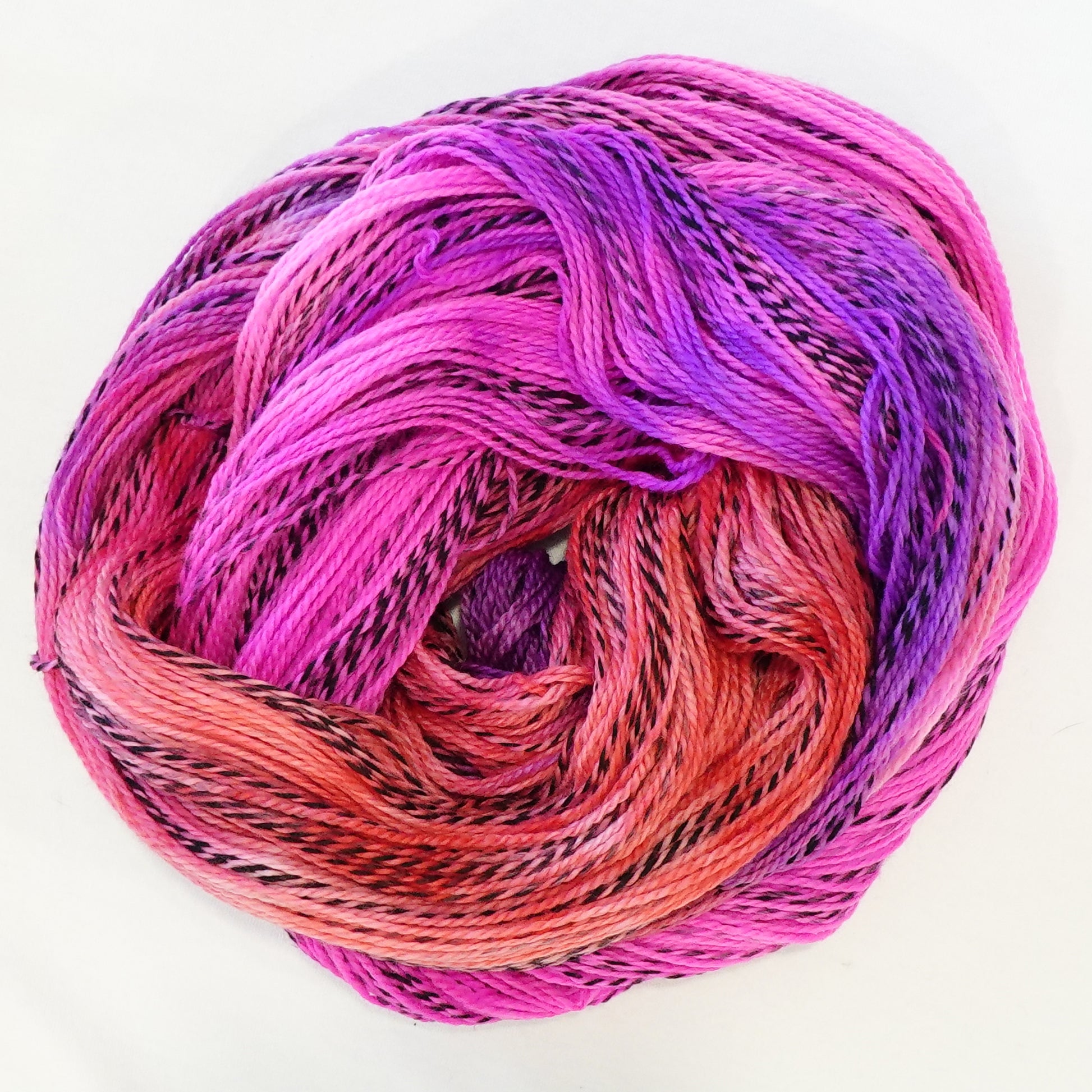 Hand-dyed fingering weight yarn in coral, hot magenta, and electric violet with black threading throughout on a zebra base.
