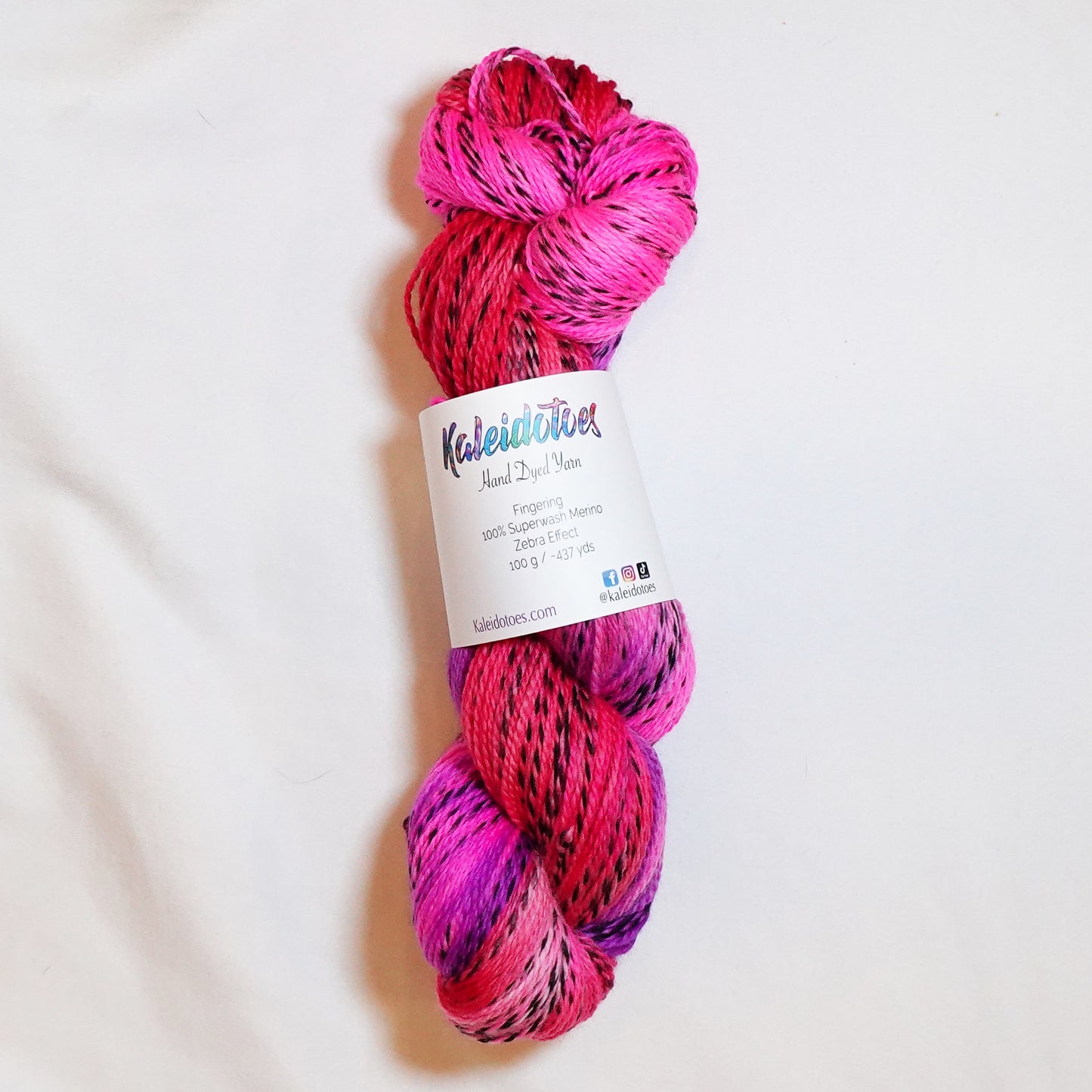 Hand-dyed fingering weight yarn in coral, hot magenta, and electric violet with black threading throughout on a zebra base.