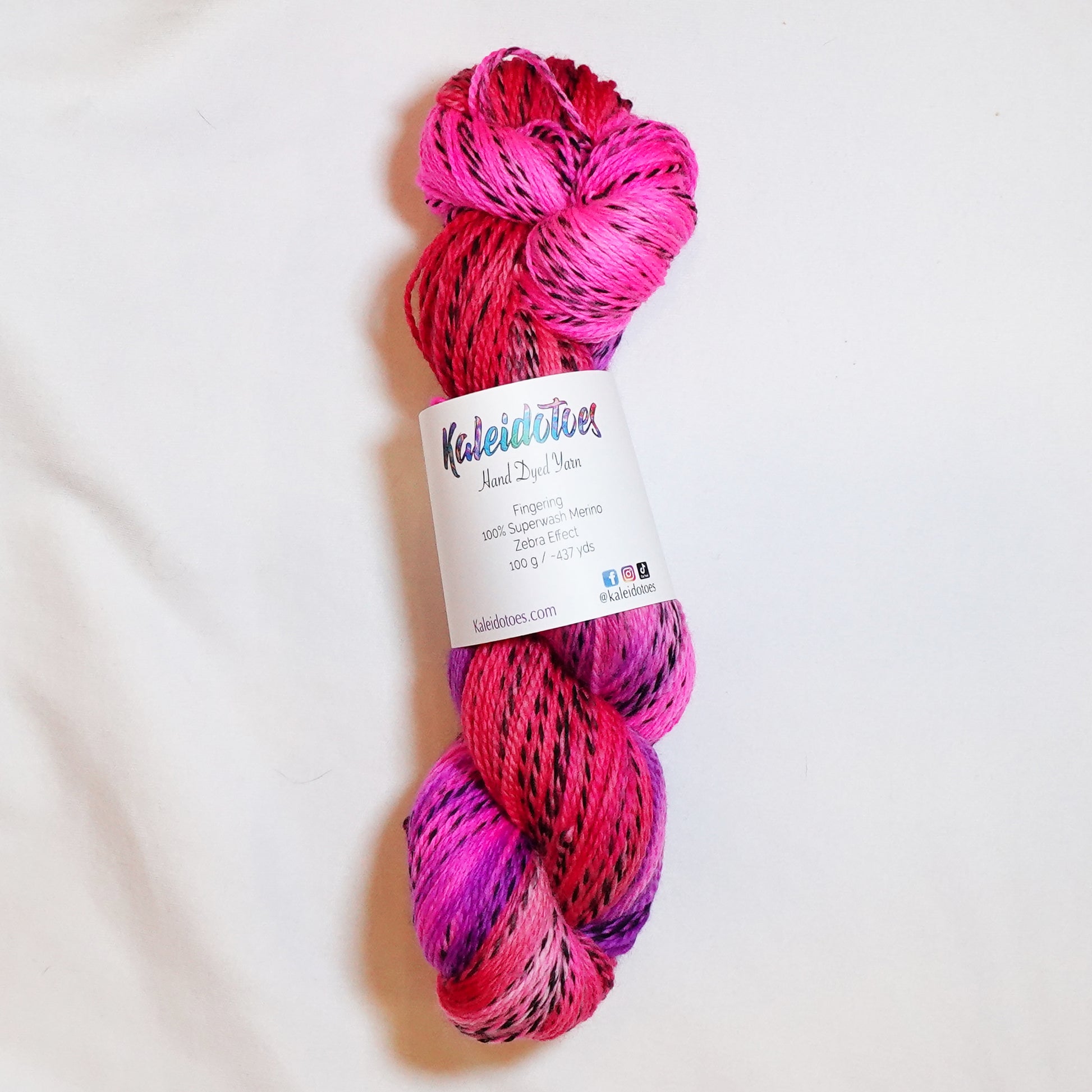 Hand-dyed fingering weight yarn in coral, hot magenta, and electric violet with black threading throughout on a zebra base.