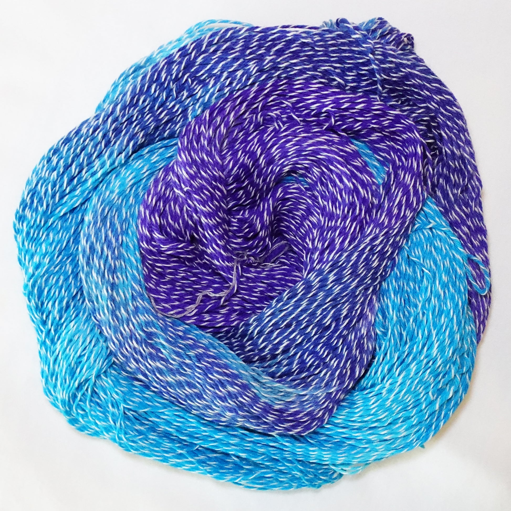Hand-dyed white zebra base fingering weight yarn in bright turquoise, deep blue, and violet purple with white plied throughout.