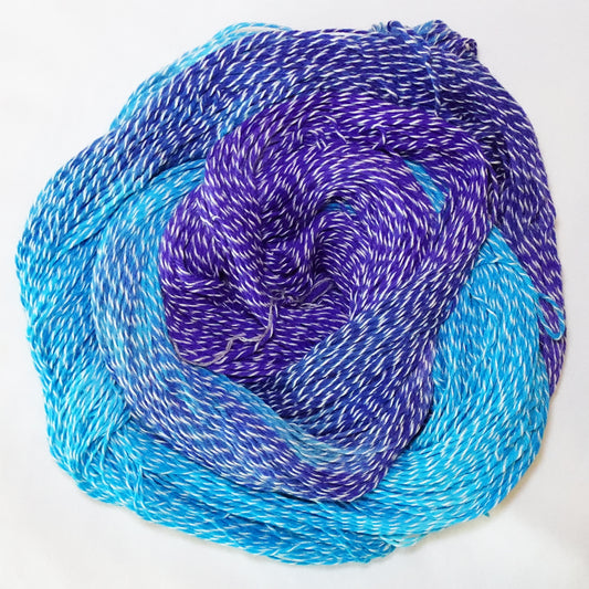 Hand-dyed white zebra base fingering weight yarn in bright turquoise, deep blue, and violet purple with white plied throughout.