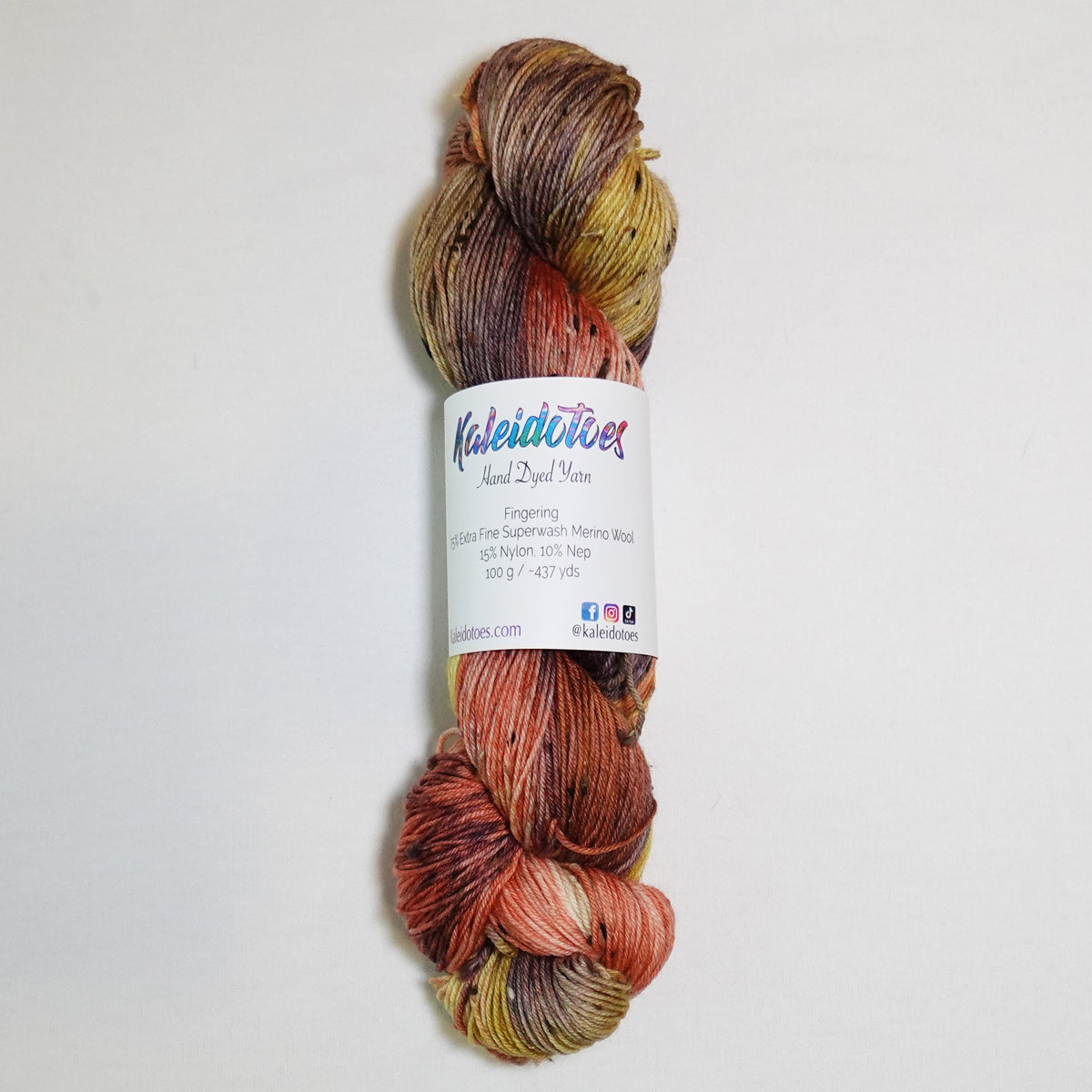 Hand-dyed tweed fingering weight yarn in burnished coral, ochre gold, earthy olive and smoky plum-brown with black tweed flecks.