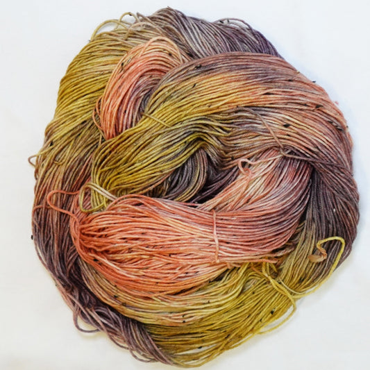Hand-dyed tweed fingering weight yarn in burnished coral, ochre gold, earthy olive and smoky plum-brown with black tweed flecks.