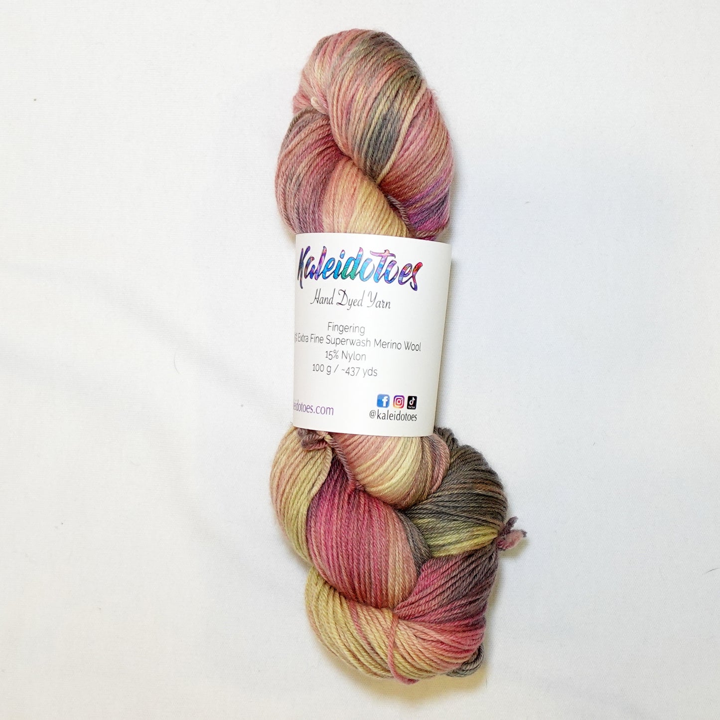 Hand-dyed fingering weight yarn in dusty rose, golden straw, muted olive, and weathered grey-brown with soft blended color transitions throughout.