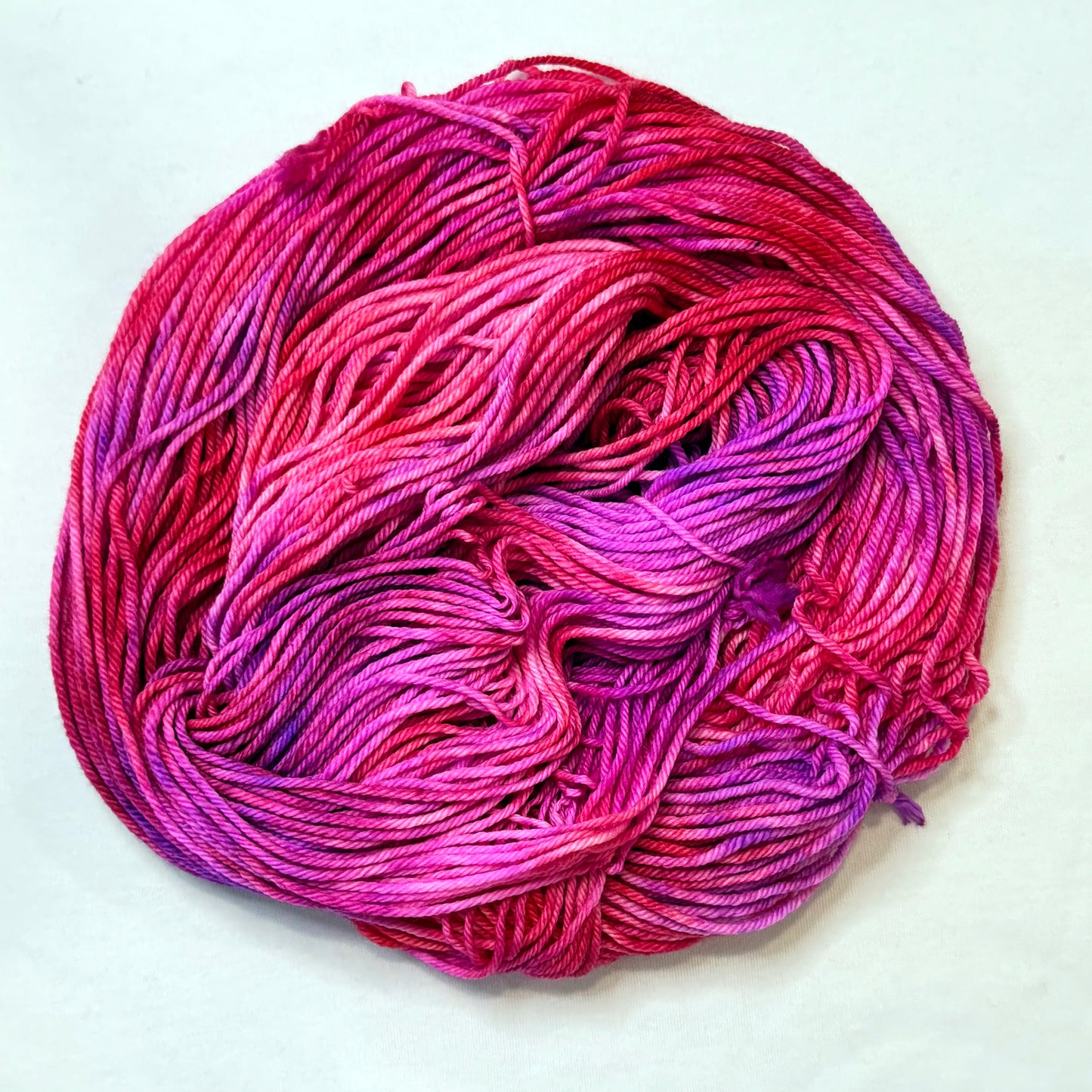 Hand-dyed yarn in a mix of bright red, pink, and purple tones 