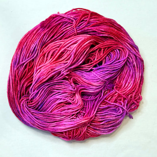 Hand-dyed yarn in a mix of bright red, pink, and purple tones 