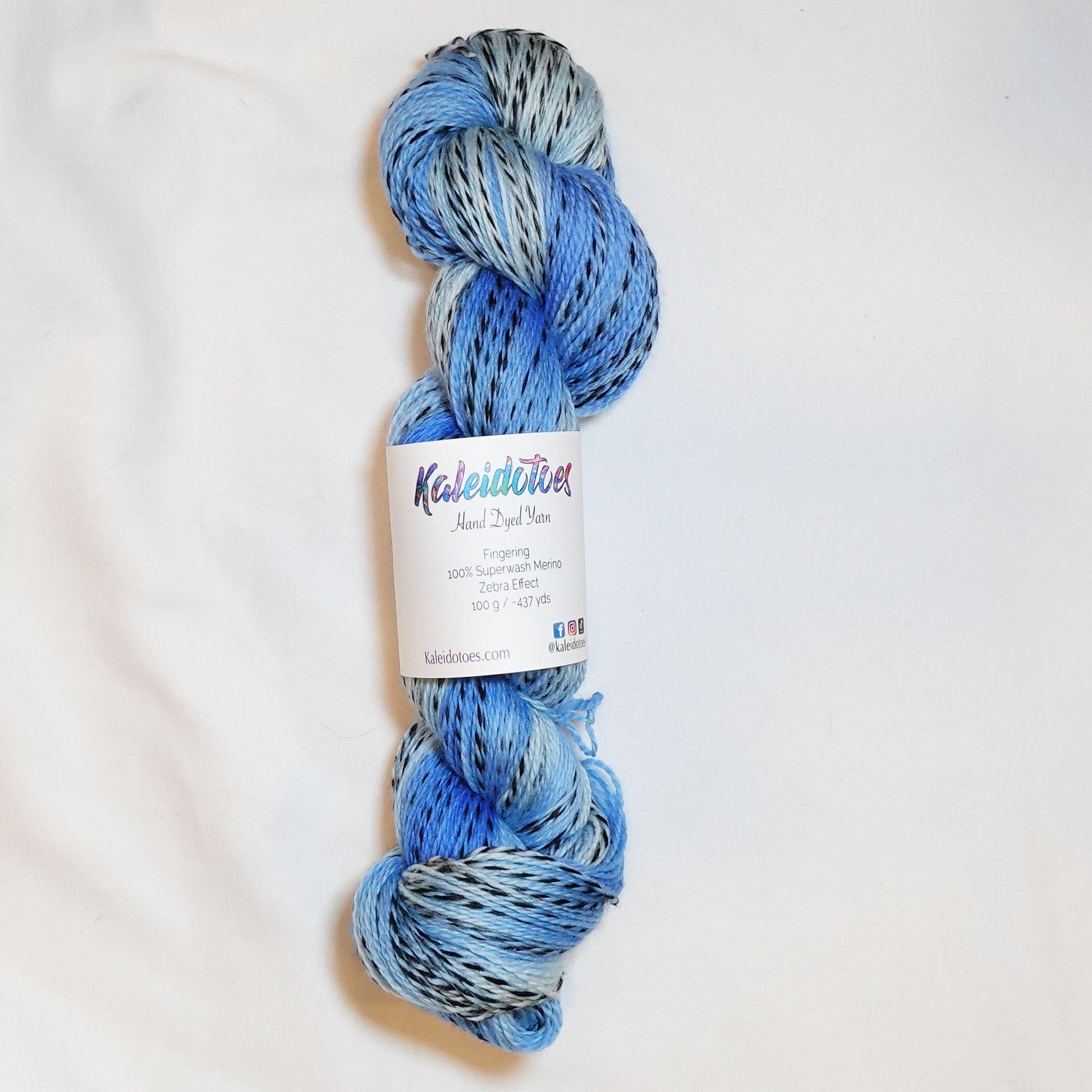 Hand-dyed fingering weight yarn in sand, sage, sky blue, and olive with black threading throughout on a zebra base.