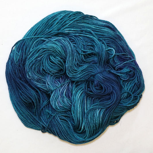 Hand-dyed worsted weight yarn in deep teal and navy blue with indigo shadow tones and lighter teal variation throughout.