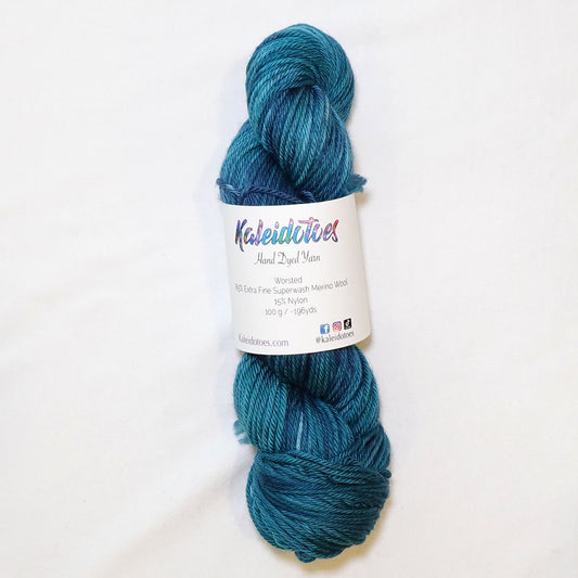 Hand-dyed worsted weight yarn in deep teal and navy blue with indigo shadow tones and lighter teal variation throughout.