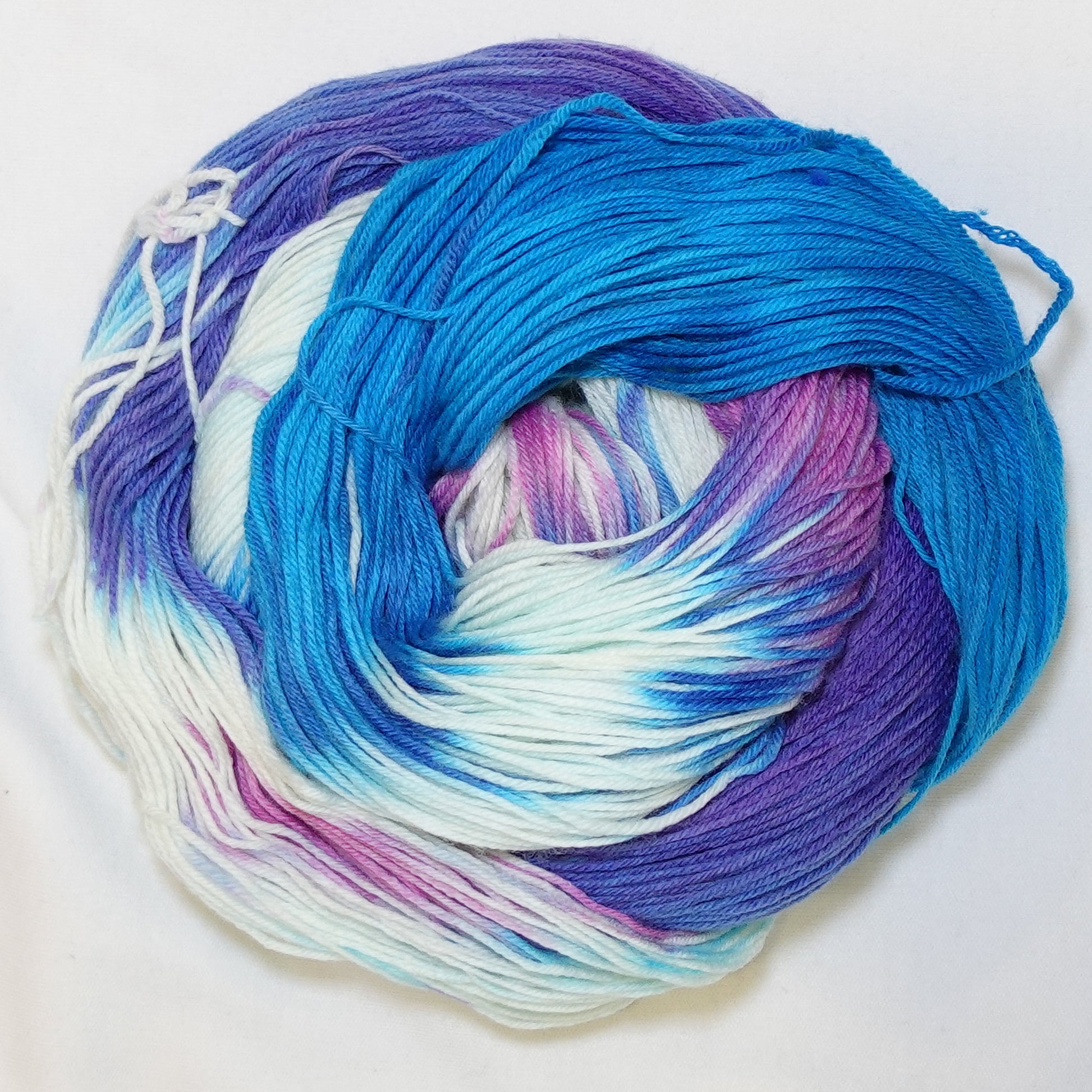 Hand-dyed fingering weight yarn in brilliant blue, soft mint, white, deep violet, and pink with swirling tie-dye color movement throughout.