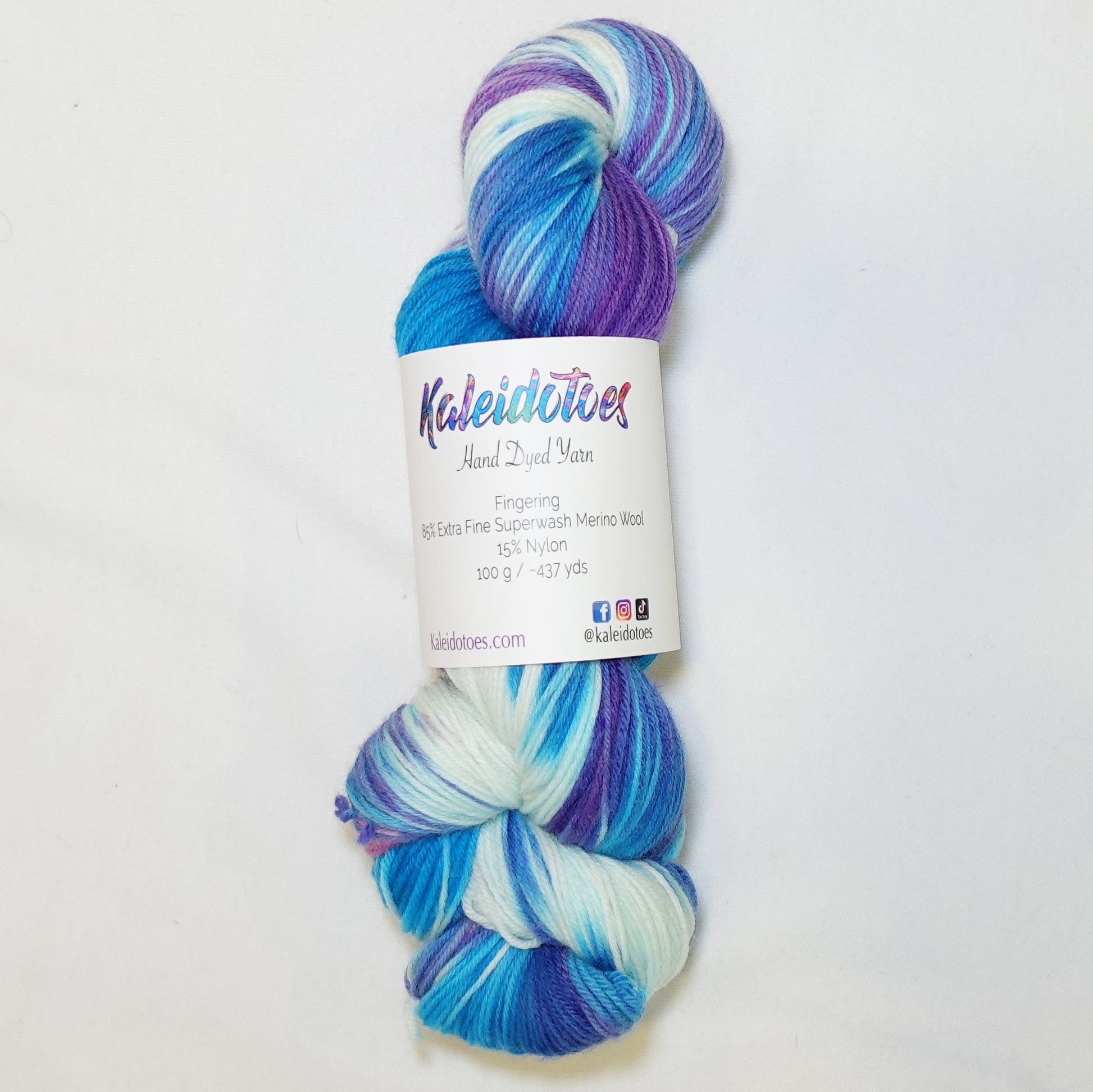 Hand-dyed fingering weight yarn in brilliant blue, soft mint, white, deep violet, and pink with swirling tie-dye color movement throughout.
