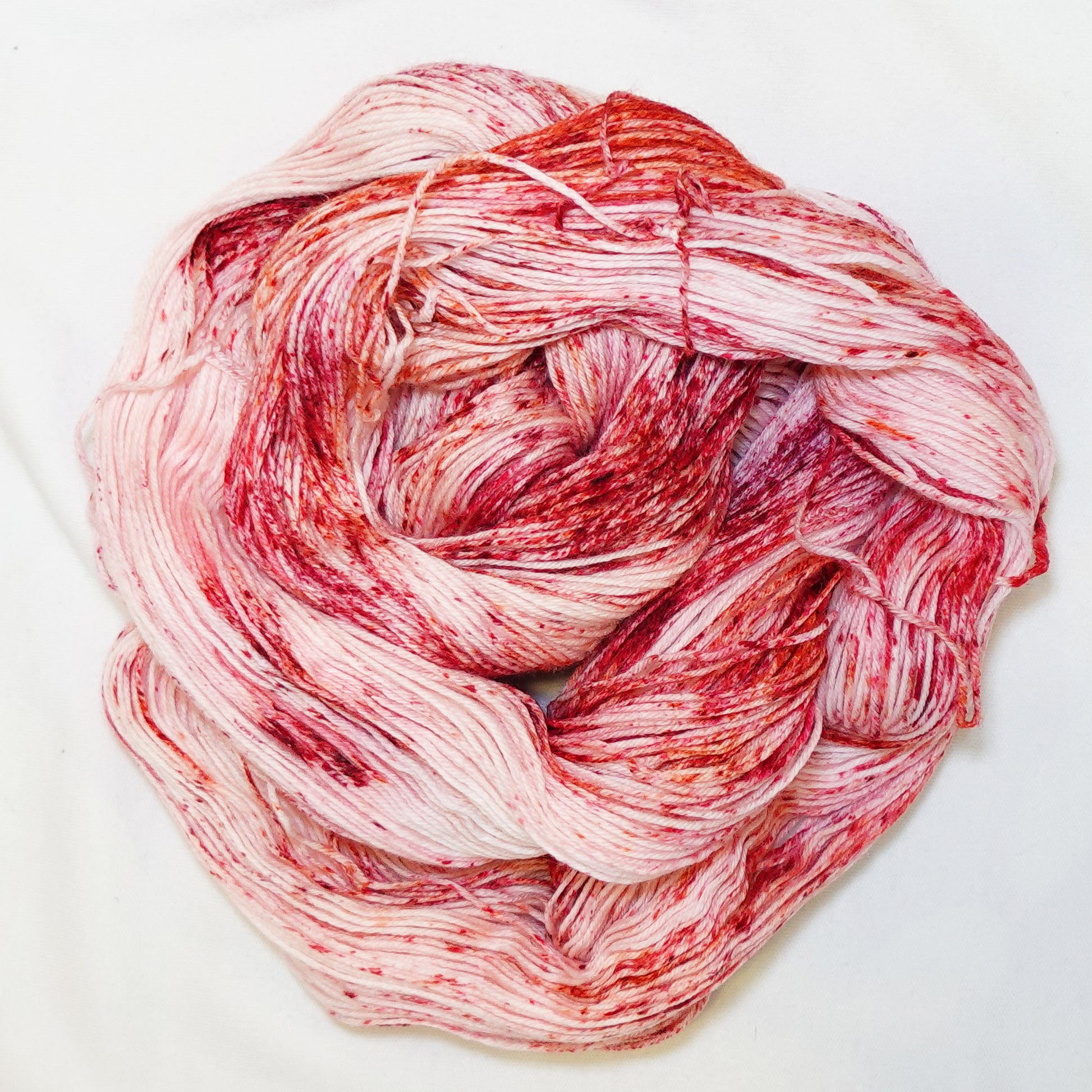 Hand-dyed fingering weight yarn in blush and cream with deep red and warm orange speckles scattered throughout.