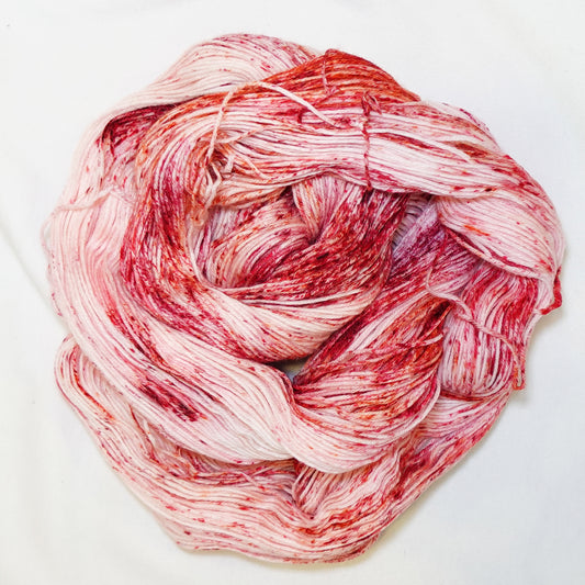 Hand-dyed fingering weight yarn in blush and cream with deep red and warm orange speckles scattered throughout.