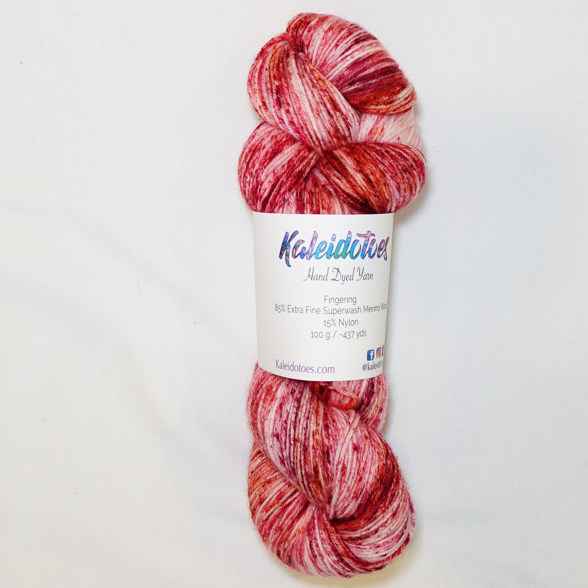 Hand-dyed fingering weight yarn in blush and cream with deep red and warm orange speckles scattered throughout.