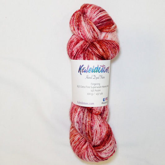 Hand-dyed fingering weight yarn in blush and cream with deep red and warm orange speckles scattered throughout.