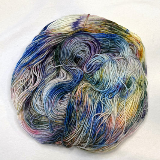 Hand-dyed yarn in soft blues, green, and pink and yellow speckles — light, floral, and garden-inspired.