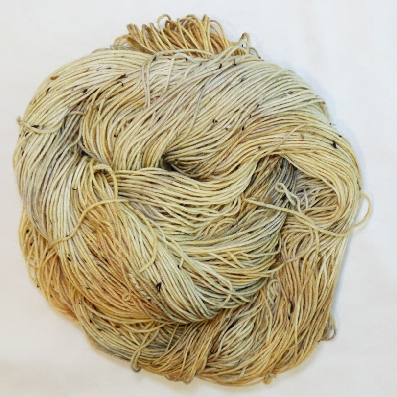 Hand-dyed tweed fingering weight yarn in weathered gold, straw, cream and soft tan with black tweed flecks.