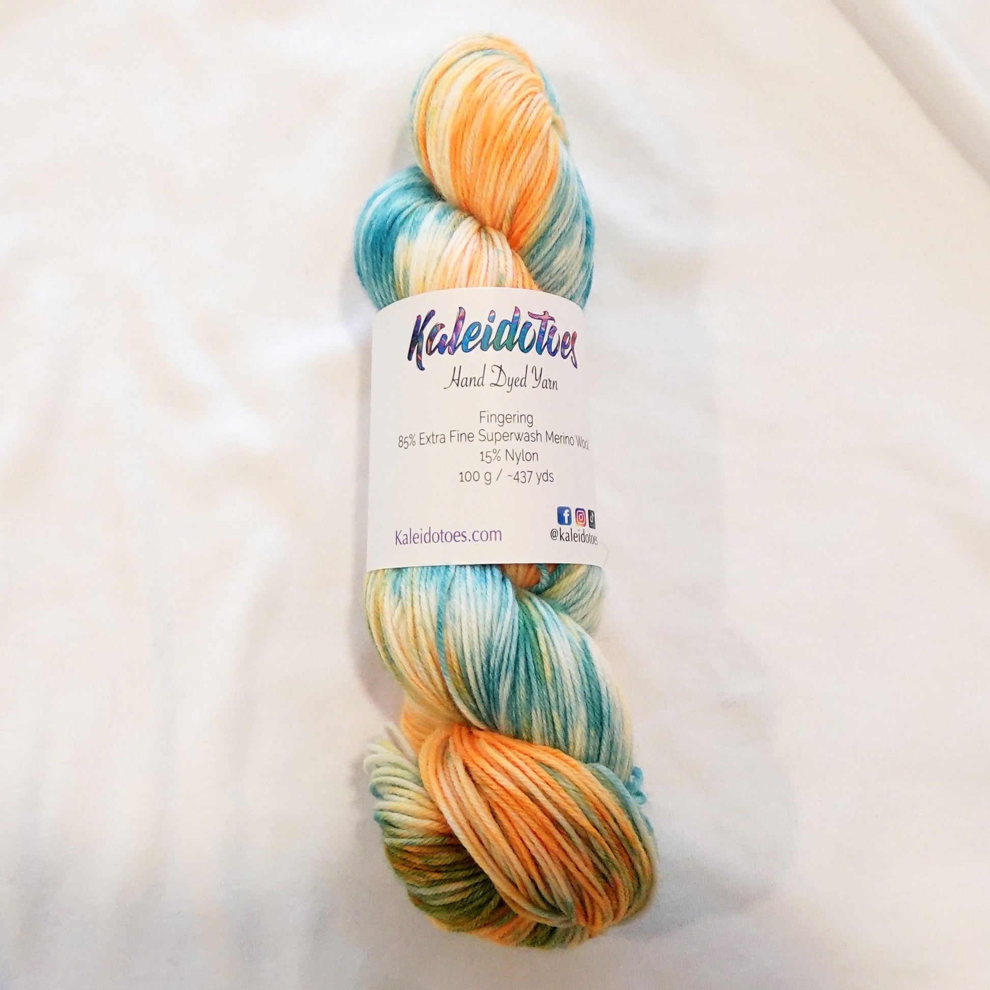 Hand-dyed fingering weight yarn in soft aqua, teal, golden orange, and cream with fluid variegated movement inspired by koi fish.