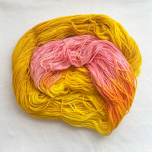 Superwash merino fingering weight yarn, variegated golden yellow with soft pink accents