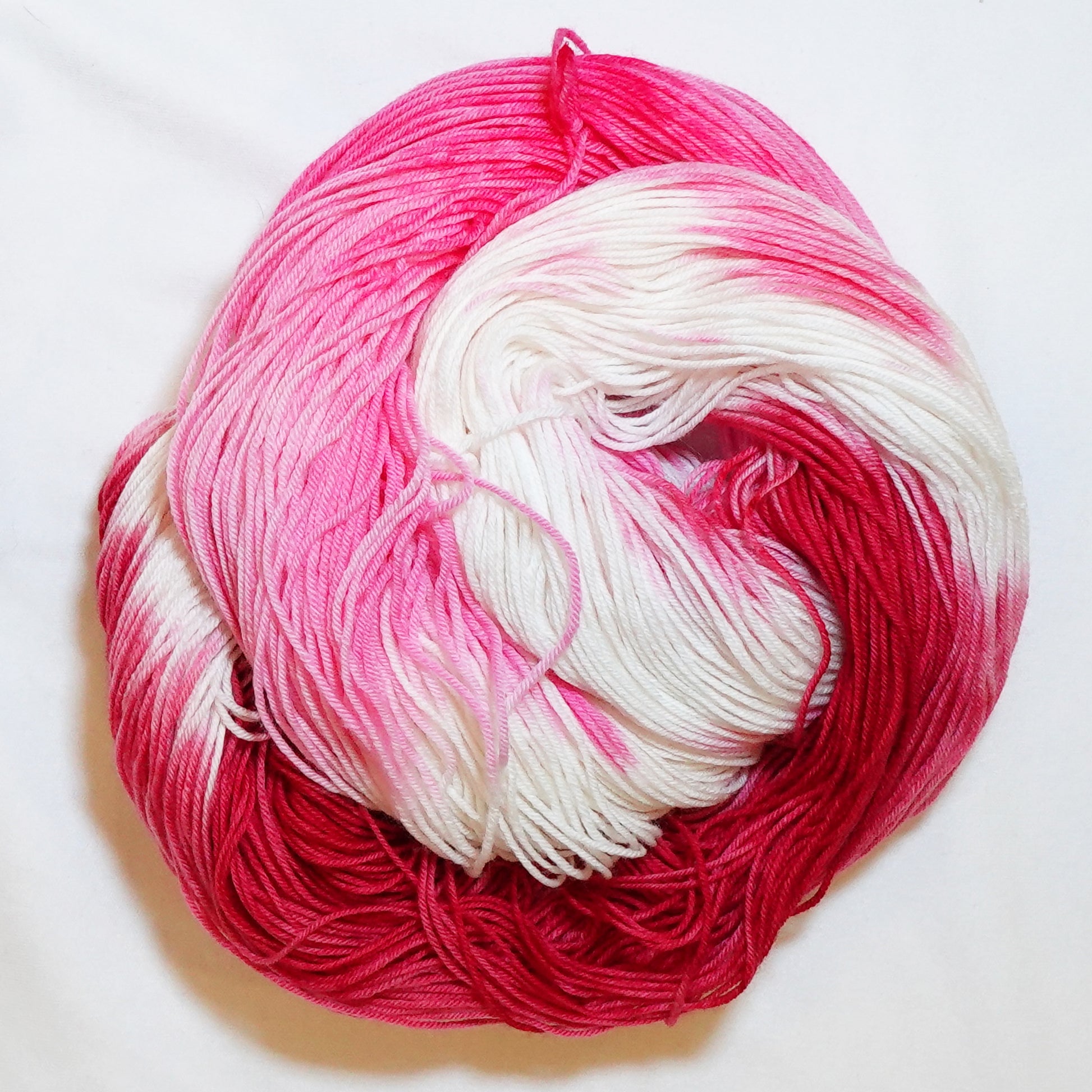 Hand-dyed fingering weight yarn in deep red, hot pink, and white with sweeping color transitions throughout.