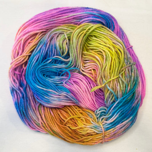 Hand-dyed yarn in shades of turquoise, pink, peach, and orchid — glowing like a tropical sunset over calm water.