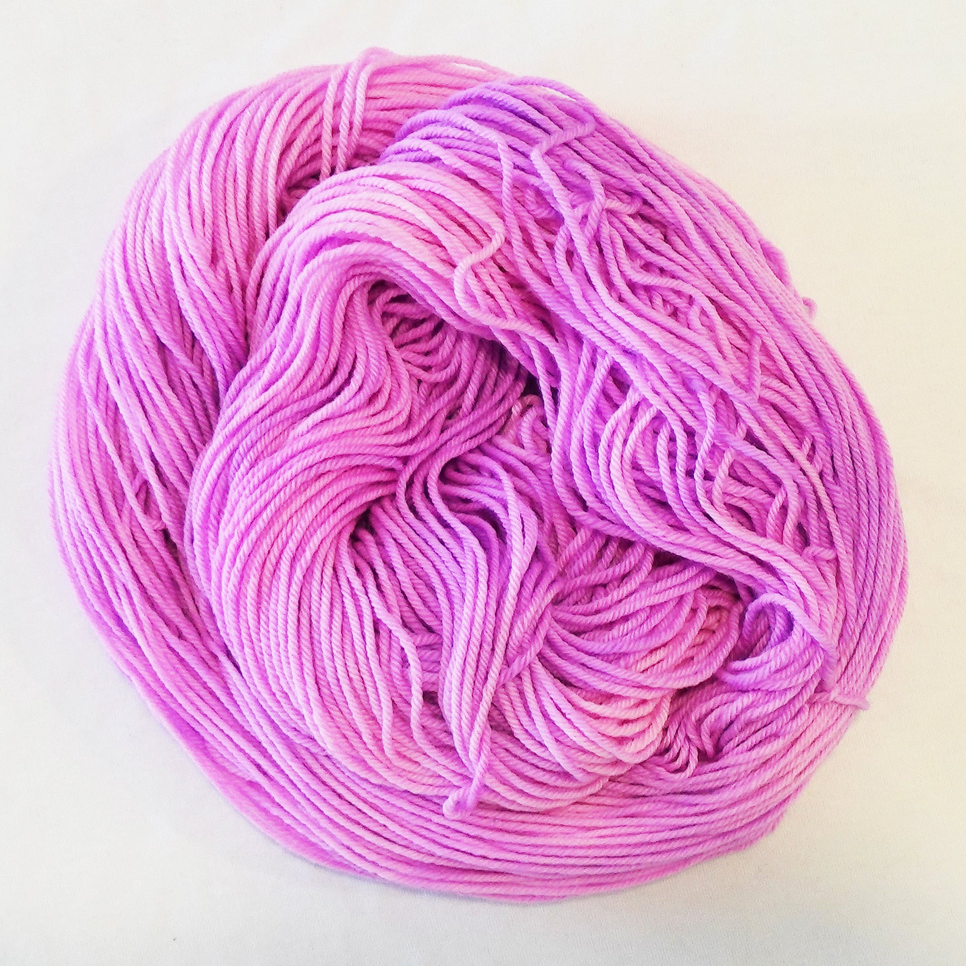 Hand-dyed yarn skein in layered cool pink tones ranging from pale blush to deeper petal pink